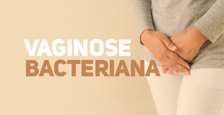 Imagem com fundo bege claro contendo o texto VAGINOSE BACTERIANA em letras maiúsculas no lado esquerdo, em duas linhas. A palavra VAGINOSE está em tom branco e a palavra BACTERIANA em tom marrom/caramelo. No lado direito, uma mulher vestindo blusa cinza de mangas compridas e calça branca é vista da cintura para baixo, segurando a região pélvica/baixo ventre com ambas as mãos.